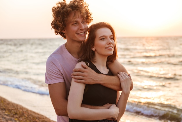 Linda joven pareja amorosa feliz abrazándose al aire libre en la playa