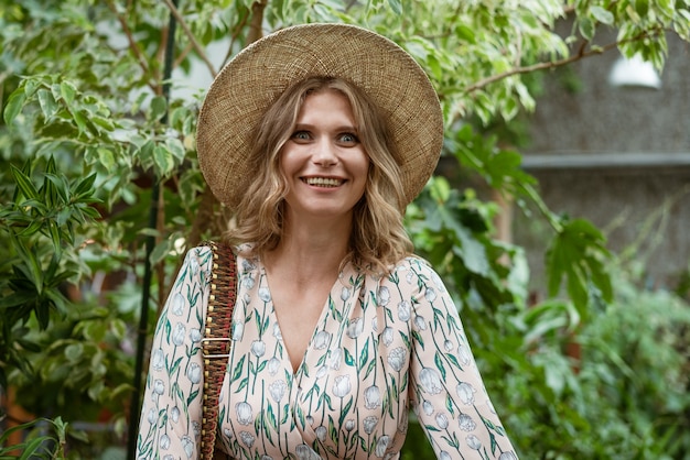 Linda joven rubia posando y sonriendo entre la vegetación en el invernadero