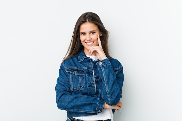 Linda joven sonriente feliz y segura, tocando la barbilla con la mano.