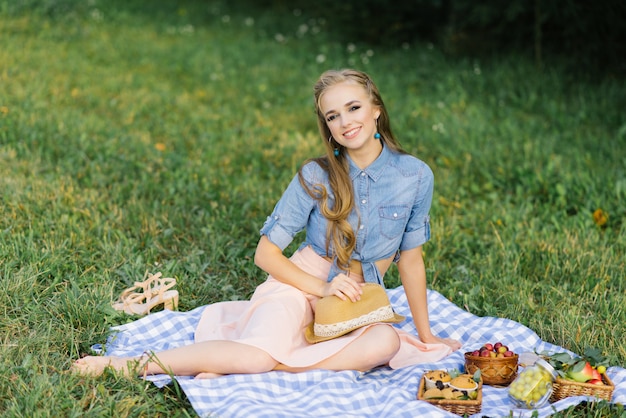 Linda joven sonriente sentada en una manta. y lleva un sombrero en un picnic de verano