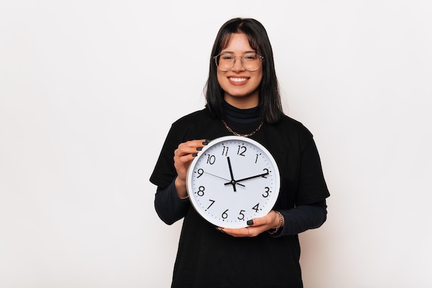 Una linda joven sonriente sostiene un reloj blanco redondo porque el tiempo vuela