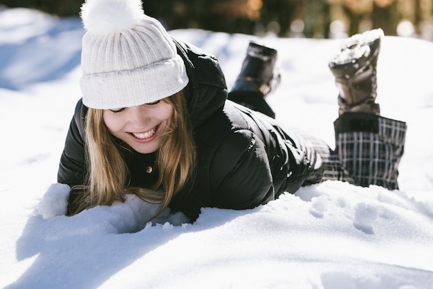 Linda jovencita acostada jugando y disfrutando de la nieve en invierno