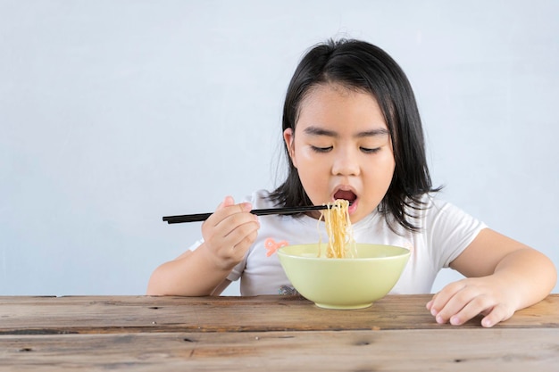Linda jovencita asiática usando palillos para comer deliciosos fideos instantáneos