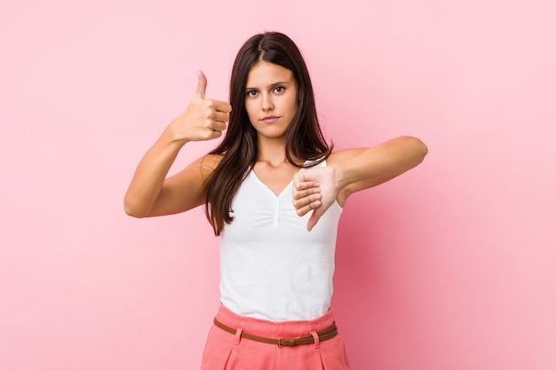 Linda jovencita mostrando los pulgares hacia arriba y hacia abajo, difícil elegir el concepto