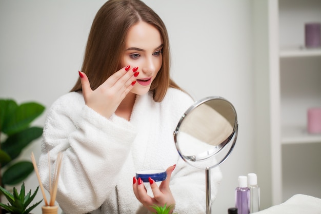 Linda jovencita pone maquillaje en la cara en el baño