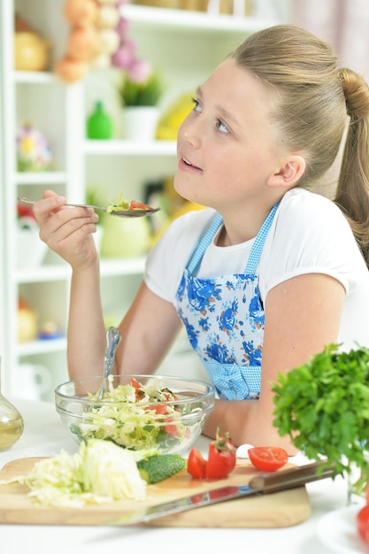 Linda jovencita preparando ensalada fresca en la mesa de la cocina