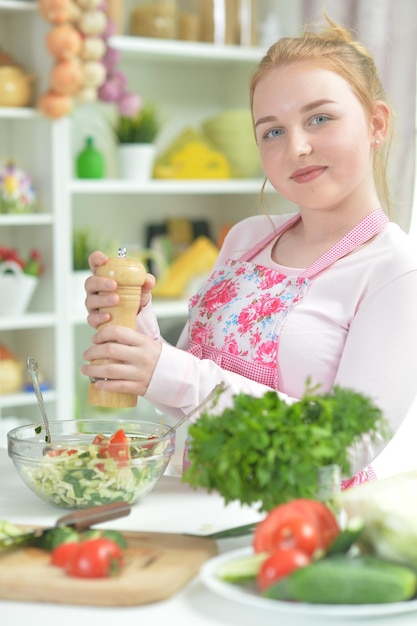 Linda jovencita preparando ensalada fresca en la mesa de la cocina