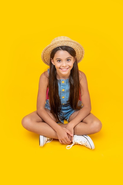 Linda jovencita con sombrero de paja sentada sobre fondo amarillo