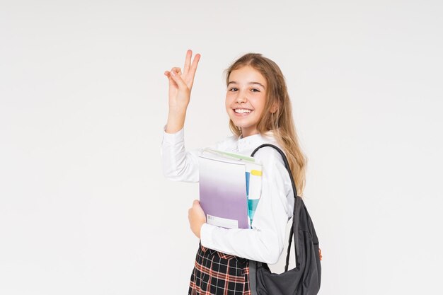 Linda jovencita sonriente en uniforme escolar con libros en sus manos aislado en el fondo blanco.