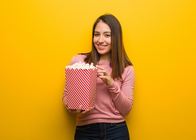 Linda jovencita sosteniendo un cubo de palomitas de maíz alegre con una gran sonrisa