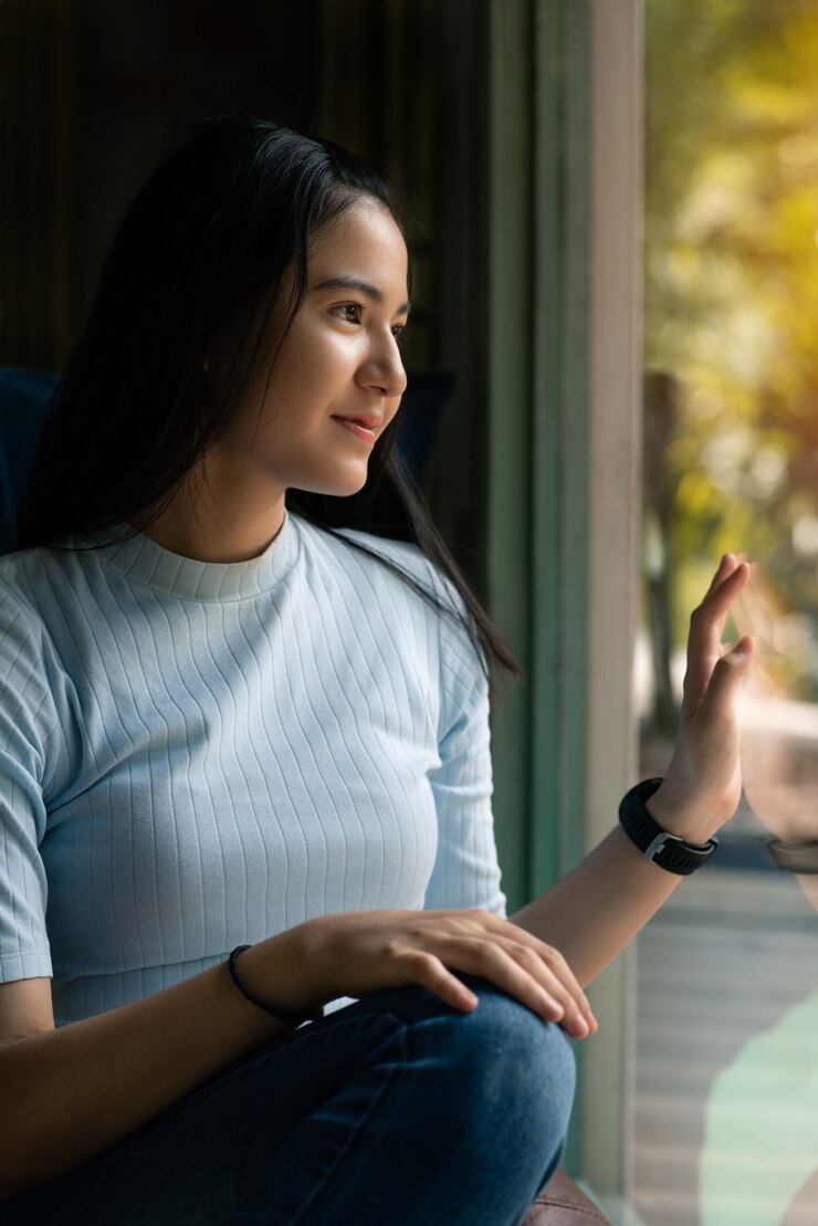 Linda linda garota asiática sentado e sorrindo no café perto da janela. Cabelo comprido preto feliz mulher asiática na camisa azul. pessoas bonitas e conceito da moda