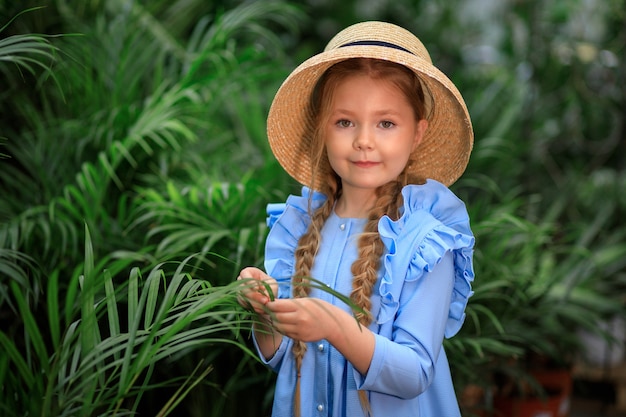 Linda linda garota com um chapéu de palha em uma estufa perto de plantas verdes