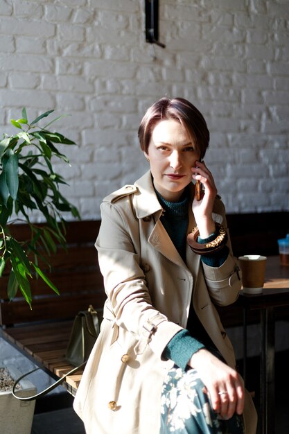 Linda linda garota no café olhando para a câmera com café sorrindo. suéter de malha verde. garota elegantemente vestida. garota olha para o telefone. mulher de negócios