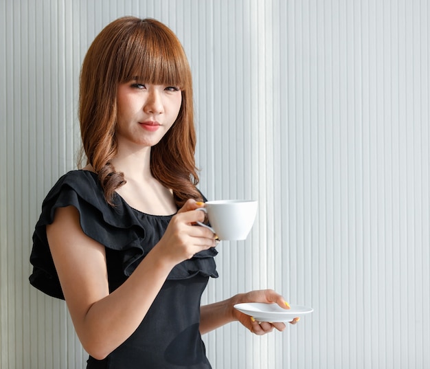 Linda linda mulher adolescente asiática segurando a xícara de café branca com uma cara feliz, conceito para o intervalo.