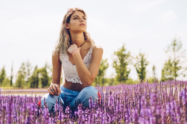 Linda loira atlética posando entre flores de sálvia