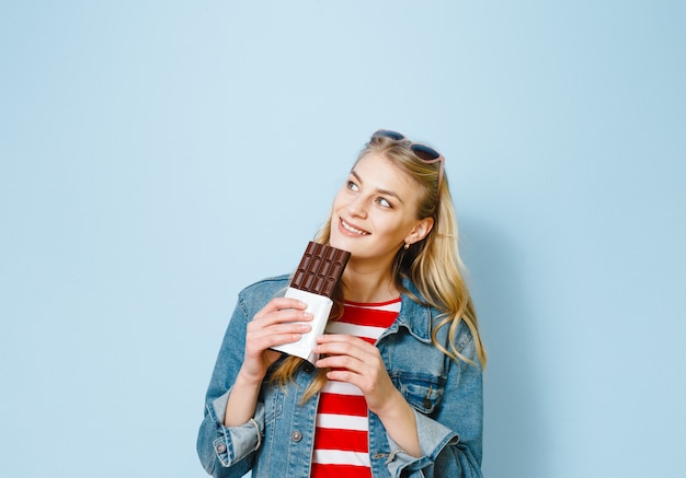 linda loira comendo chocolate está animado sobre um fundo azul