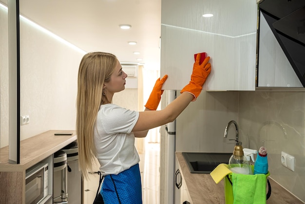 Linda loira em luvas especiais na cozinha limpa a superfície com um pano