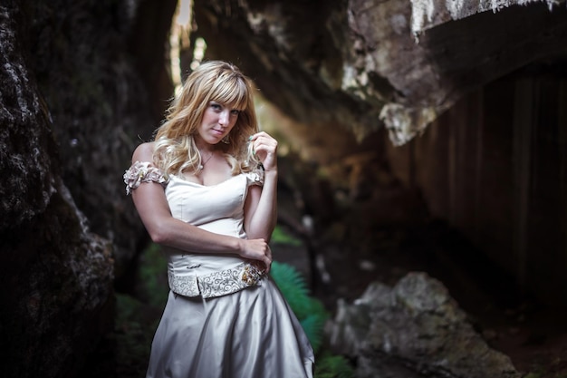 Linda loira em um vestido branco com um espartilho em uma caverna escura profunda