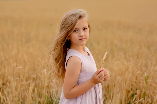 linda loira em um vestido de linho rosa fica em um campo de trigo e a toca com as mãos