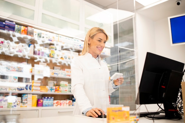 Foto linda loira farmacêutica feminina em pé na loja da farmácia e vendendo medicamentos.