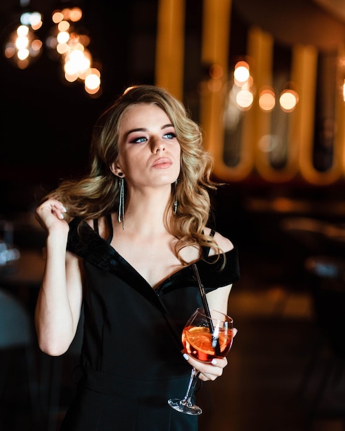 Linda loira jovem segurando um spritz de aperol Cocktail aperol spritz em um copo Retrato de uma jovem em um restaurante Retrato de uma menina Jovem em um restaurante com um copo