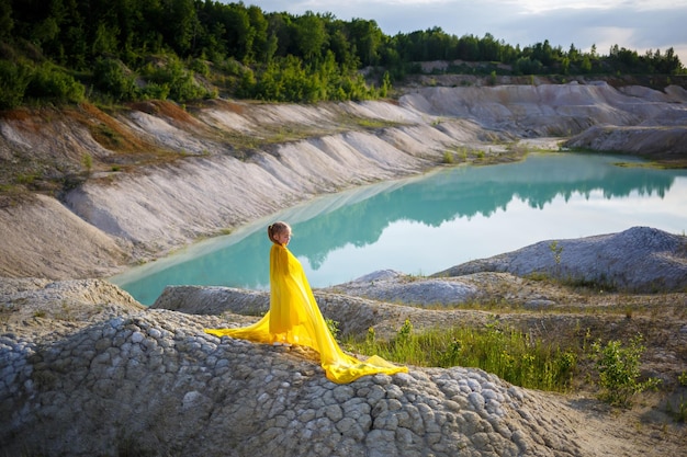 Linda loira posando com um vestido amarelo na natureza. Foto de verão. Céu azul. Dia ensolarado.