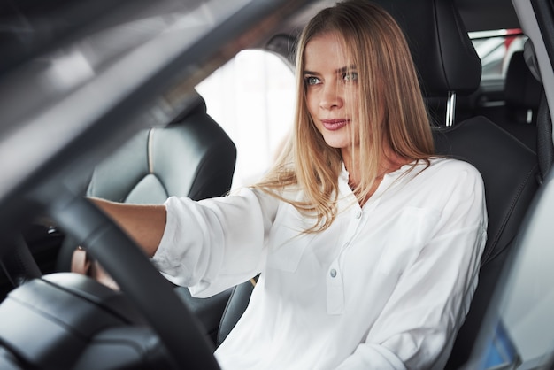 Linda loira sentada no carro novo com interior preto moderno