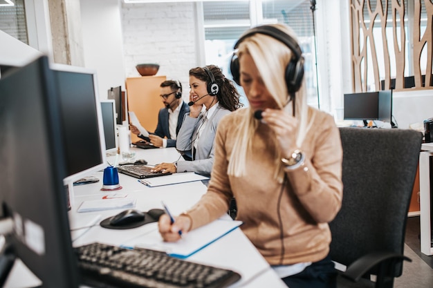 Linda loira sorridente trabalhadora de call center acompanhada por sua equipe trabalhando no escritório.