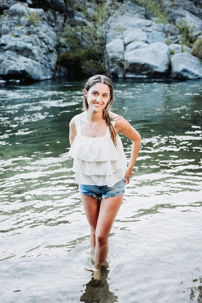 Linda loira, usando uma camiseta branca e um short jeans azul em um espaço natural, à beira do rio