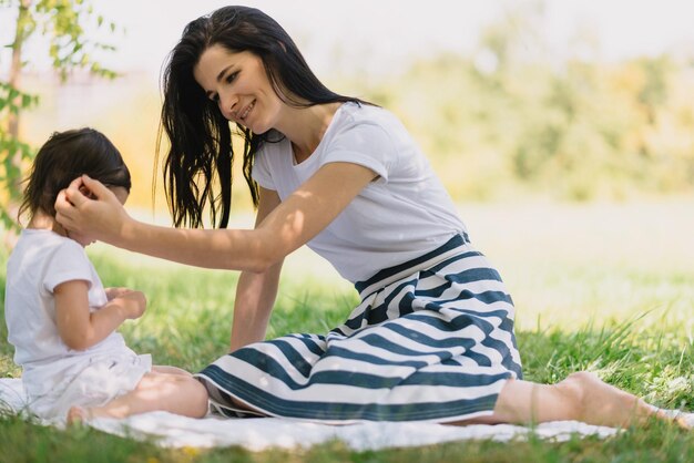 Linda madre y su linda hijita cuidando y jugando al aire libre en la hierba verde Linda madre y su alegre hijo se divierten juntos en el parque Retrato de familia feliz Maternidad e infancia