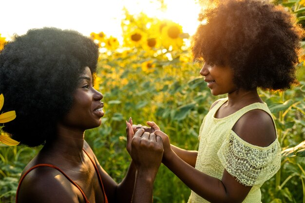 Linda mãe afro-americana e filha brincando e se divertindo em um campo de girassóis