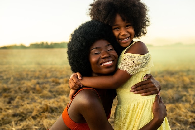 Foto linda mãe afro-americana e filha brincando e se divertindo em um campo de girassóis