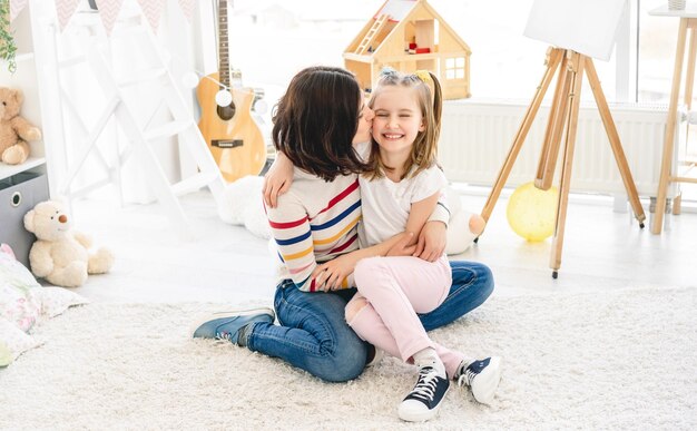 Foto linda mãe beijando menina bonitinha no quarto de crianças brilhantes