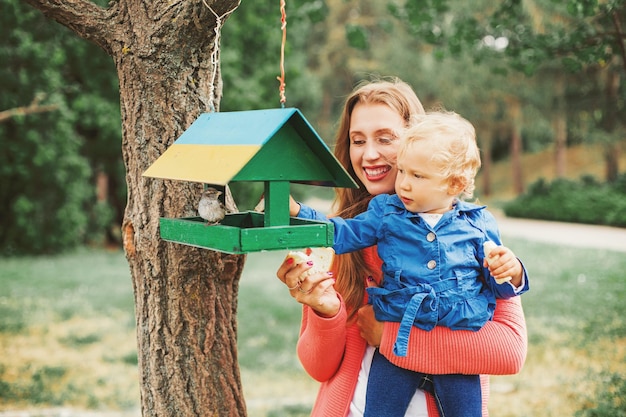 Linda mãe caucasiana e filha alimentando pássaros no parque