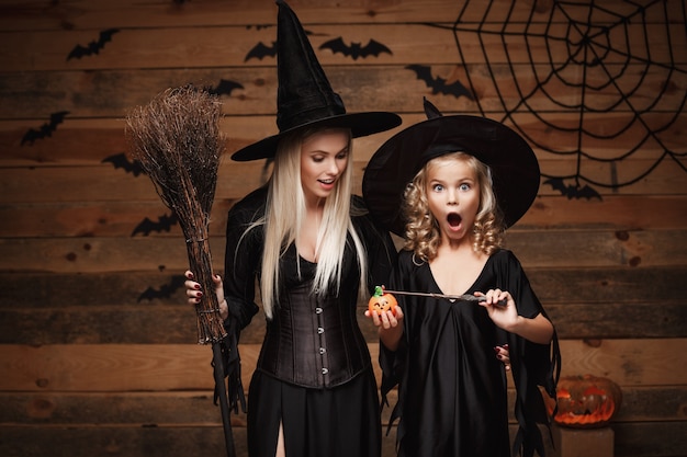 linda mãe caucasiana e sua filha em trajes de bruxa gostam de usar magia com varinha mágica para o frasco de abóbora de Halloween