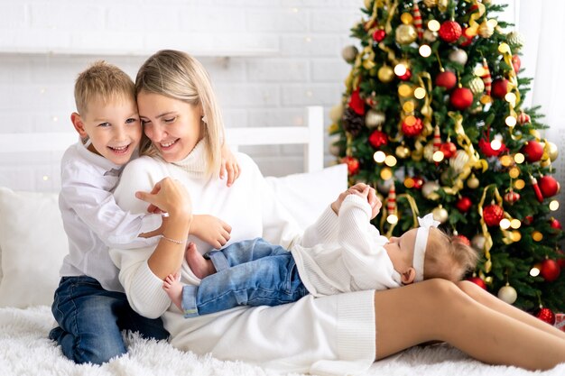 Linda mãe com dois filhos celebrando o Natal de Ano Novo em casa com a árvore de Natal