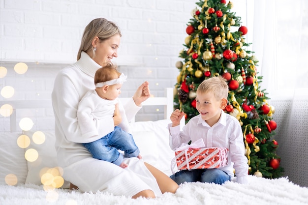 linda mãe com dois filhos dando presentes de ano novo em casa, debaixo da árvore, celebrando o Natal