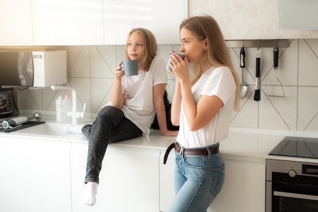 linda mãe com filha na cozinha com canecas