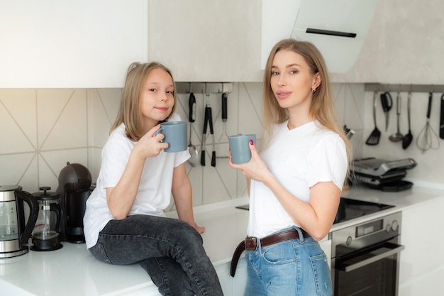 linda mãe com filha na cozinha com canecas