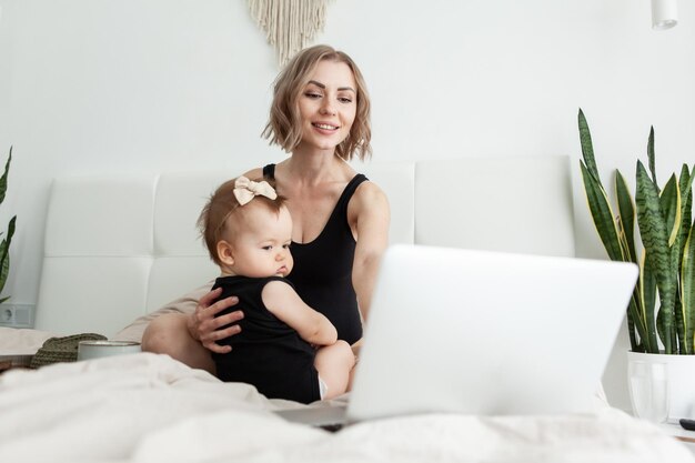 Linda mãe com sua filhinha está assistindo a um vídeo ou filme no laptop e tomando café da manhã na cama Família feliz Passar um tempo juntos Amor e carinho