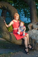 Linda mãe com um filho sentado em uma árvore no parque no verão