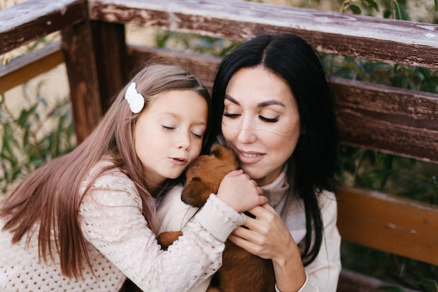 Linda mãe e filha abraçam seu cachorrinho marrom