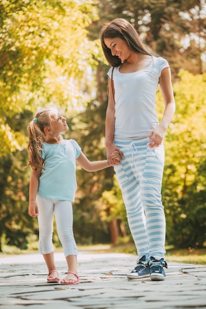 Linda mãe e filha andando por um parque na primavera.