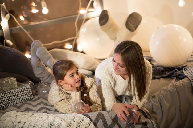 Linda mãe e filha deitada na cama na véspera de Natal no aconchegante interior da casa Ano Novo