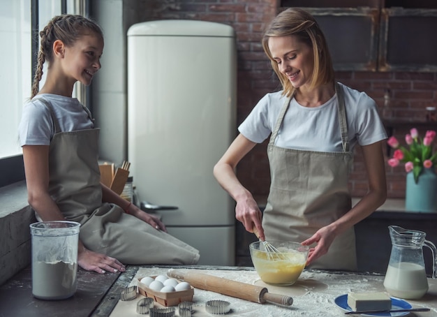 Linda mãe e filha em aventais estão fazendo biscoitos em casa mãe está batendo ovos