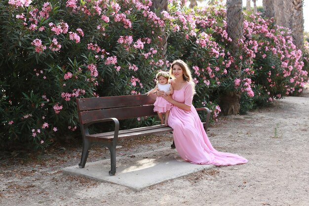 Foto linda mãe e filha em vestidos semelhantes no parque perto das flores em um dia ensolarado de verão