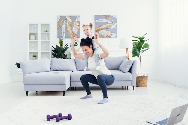 Linda mãe e filha estão sorrindo enquanto faz exercícios de fitness juntos em casa