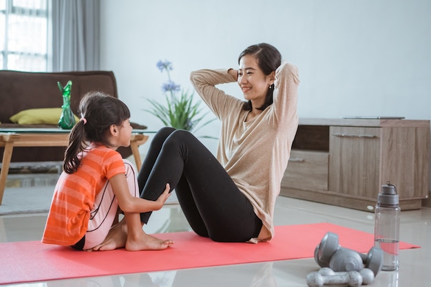 Linda mãe e filha fazendo exercícios esportivos em casa com a filha dela juntas