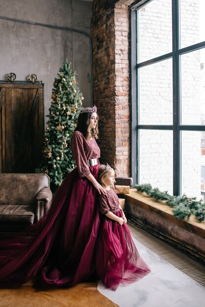 Linda mãe e filha na imagem da rainha e da princesa no vestido cor de Marsala com cauda longa no loft