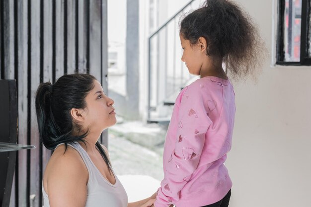 Linda mãe latina sentada no chão enquanto olha sua filha de pele marrom nos olhos